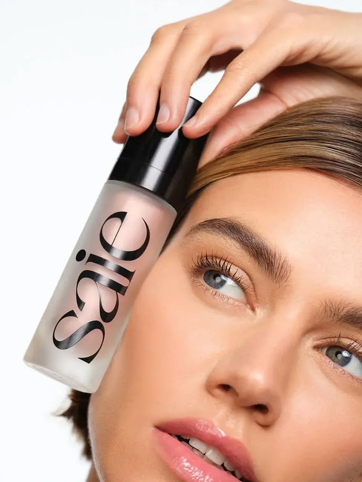 Woman holding a Saie bottle beside her face
