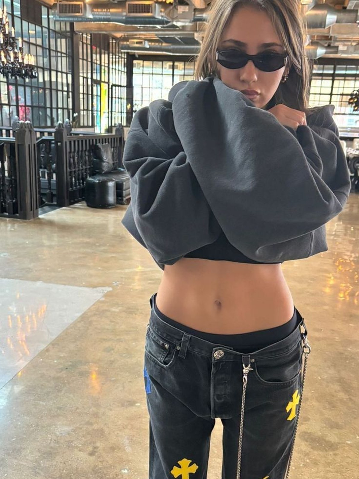 Woman in a gray sweatshirt and dark jeans with yellow cross patches