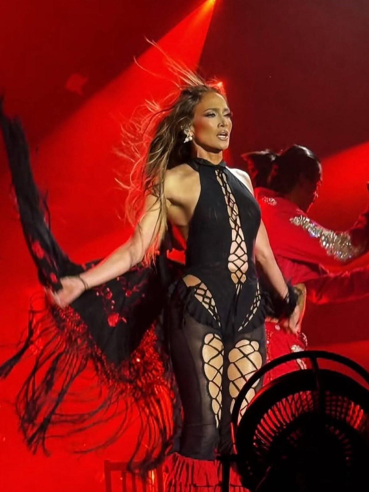 Jennifer Lopez performing in a black AMOR MIA jumpsuit under red stage lights