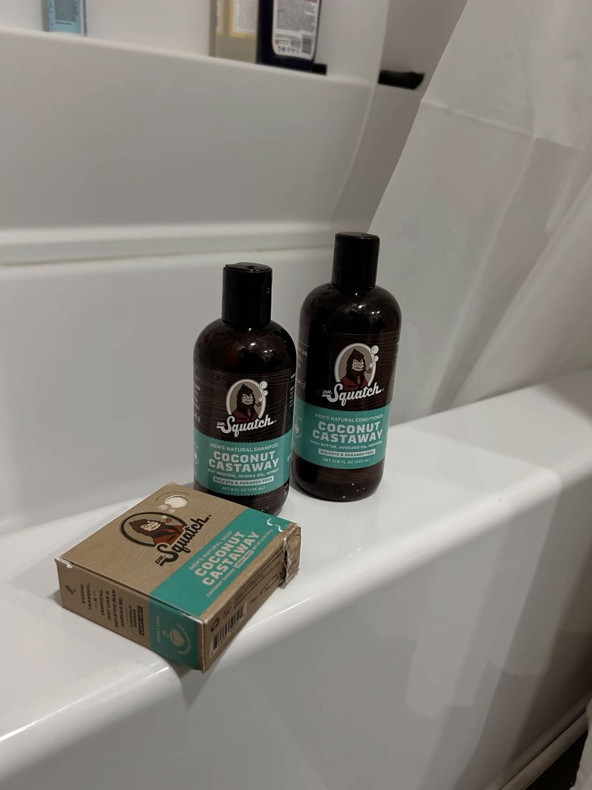 Dr. Squatch Coconut Castaway shampoo, conditioner and bar soap box on a bathtub ledge