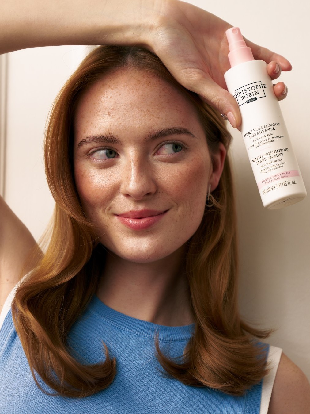 Red-haired woman holding Christophe Robin volumizing mist in a pale studio