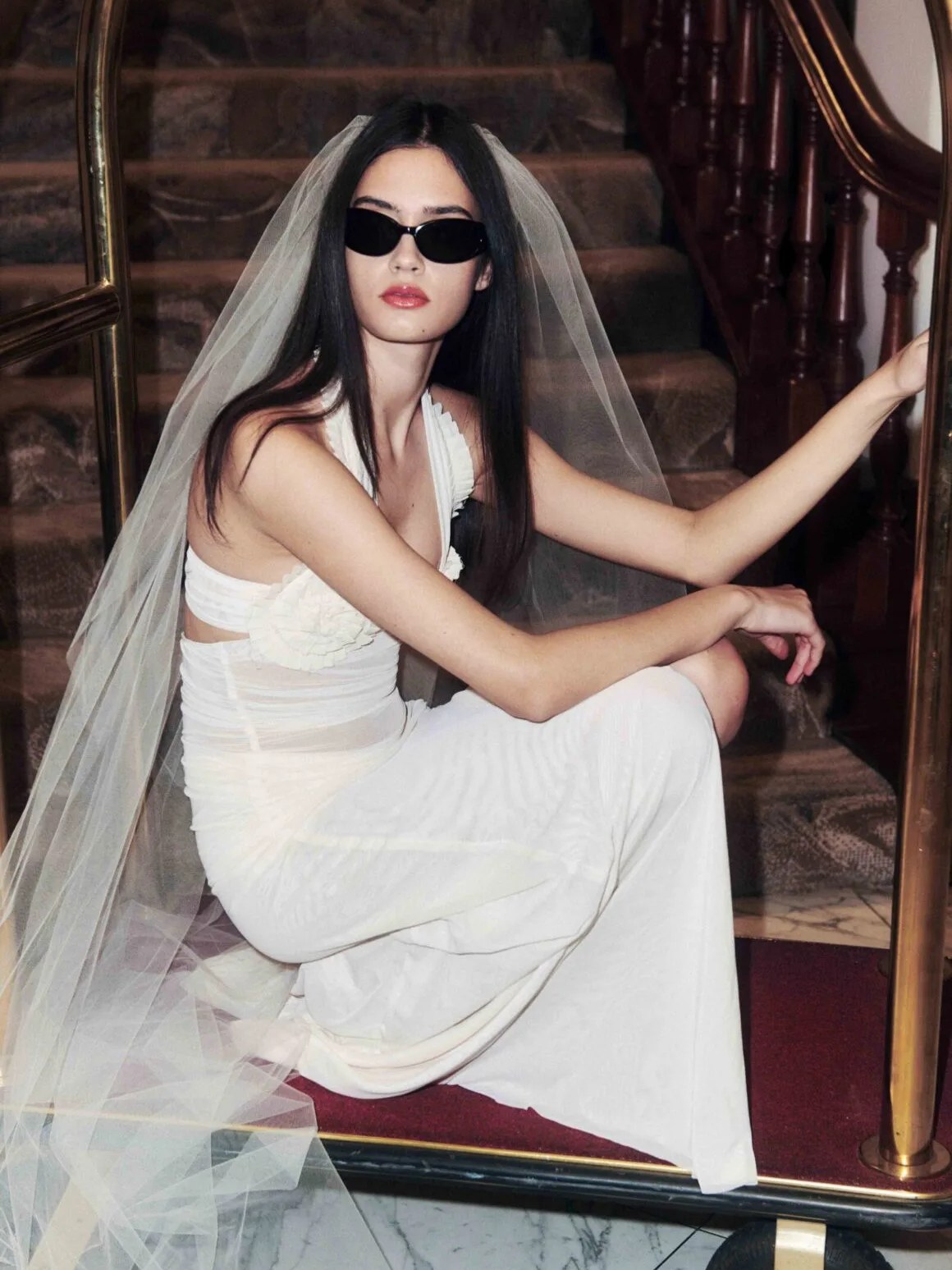 Model in a white bridal look seated on a luggage cart