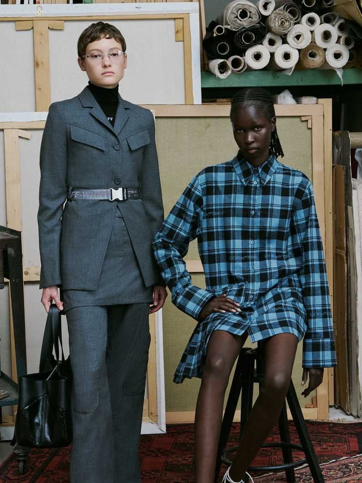 Two models in grey belted tailoring and a blue plaid shirt dress in an art studio