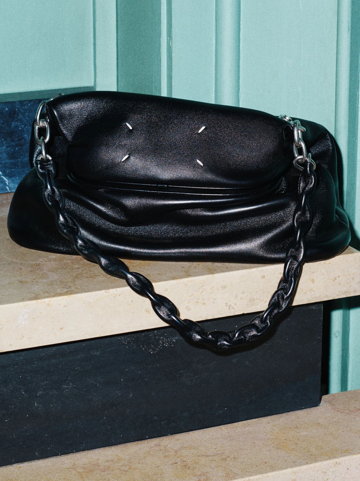 Black leather chain handle bag on stone steps against a teal wall