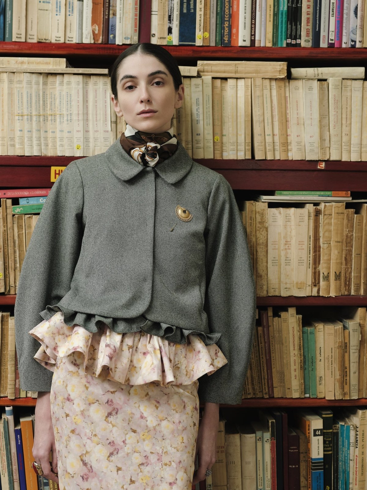 Model in a grey jacket and floral skirt among tall bookshelves