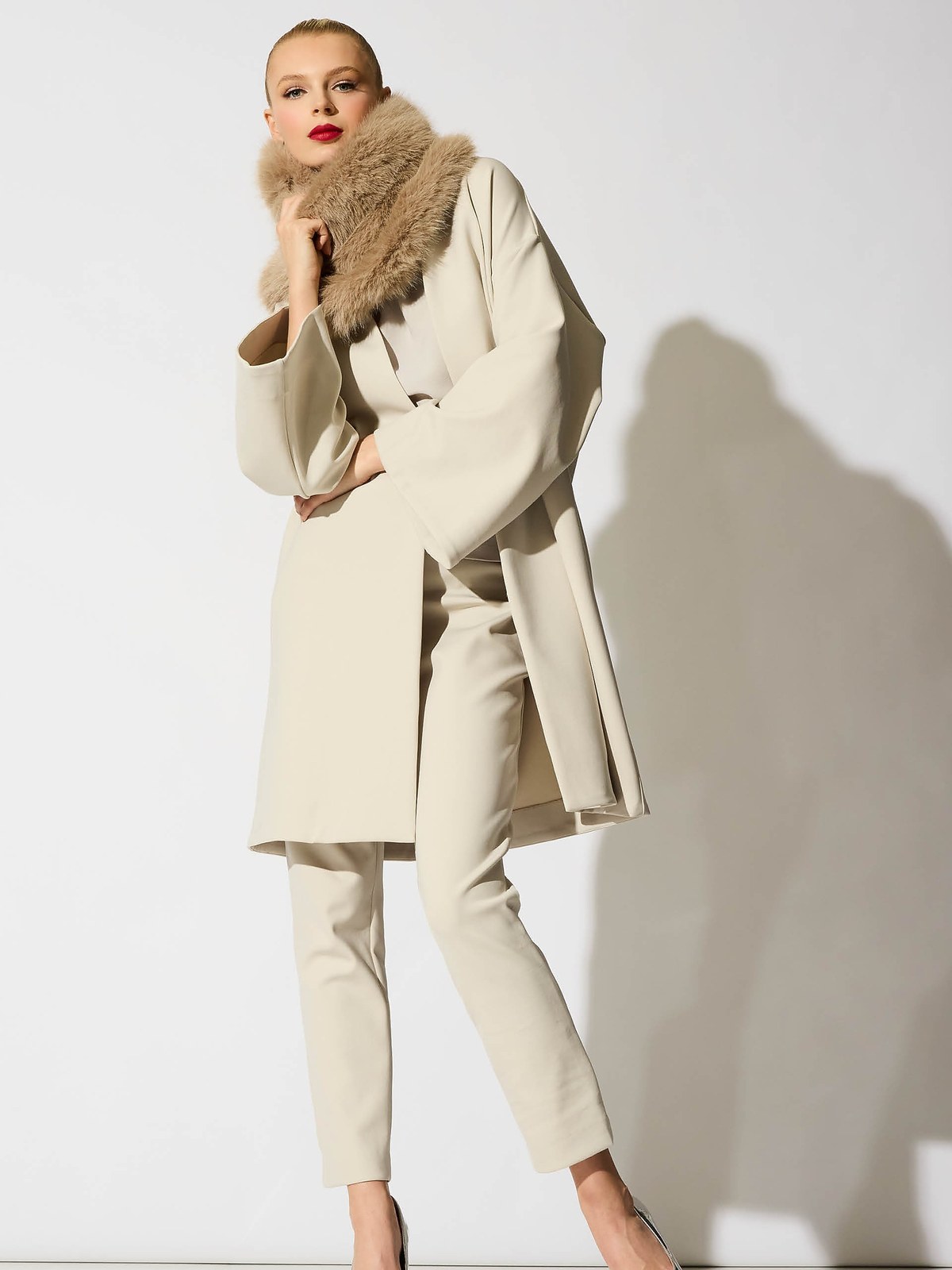 Model in a cream coat with a plush collar in a studio