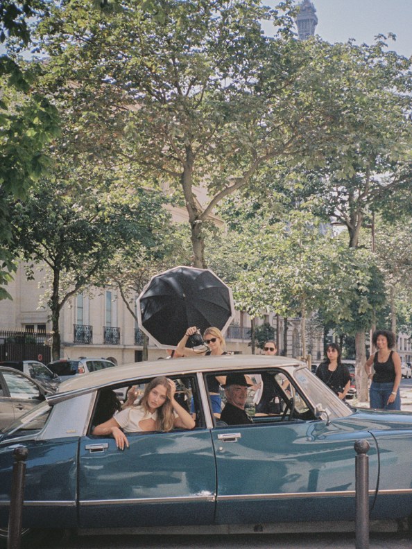 Women gather around a vintage car during the Sage’s Rose campaign in Paris