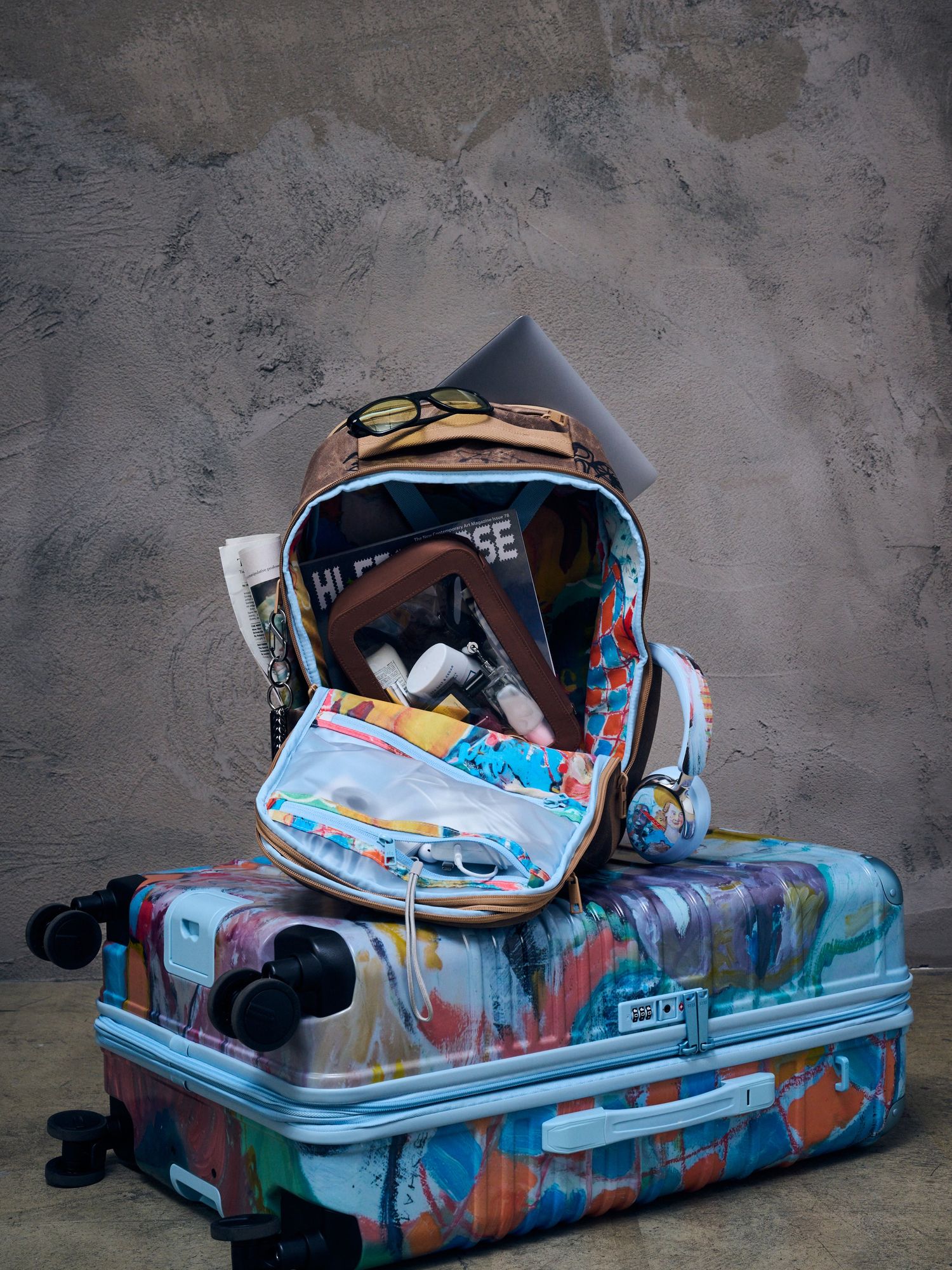 Open painted backpack and contents on a painted suitcase on concrete