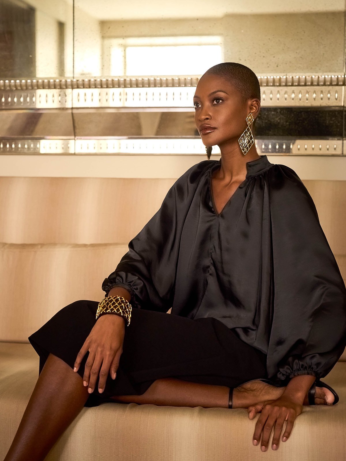Model in a black satin blouse and skirt seated on a sofa