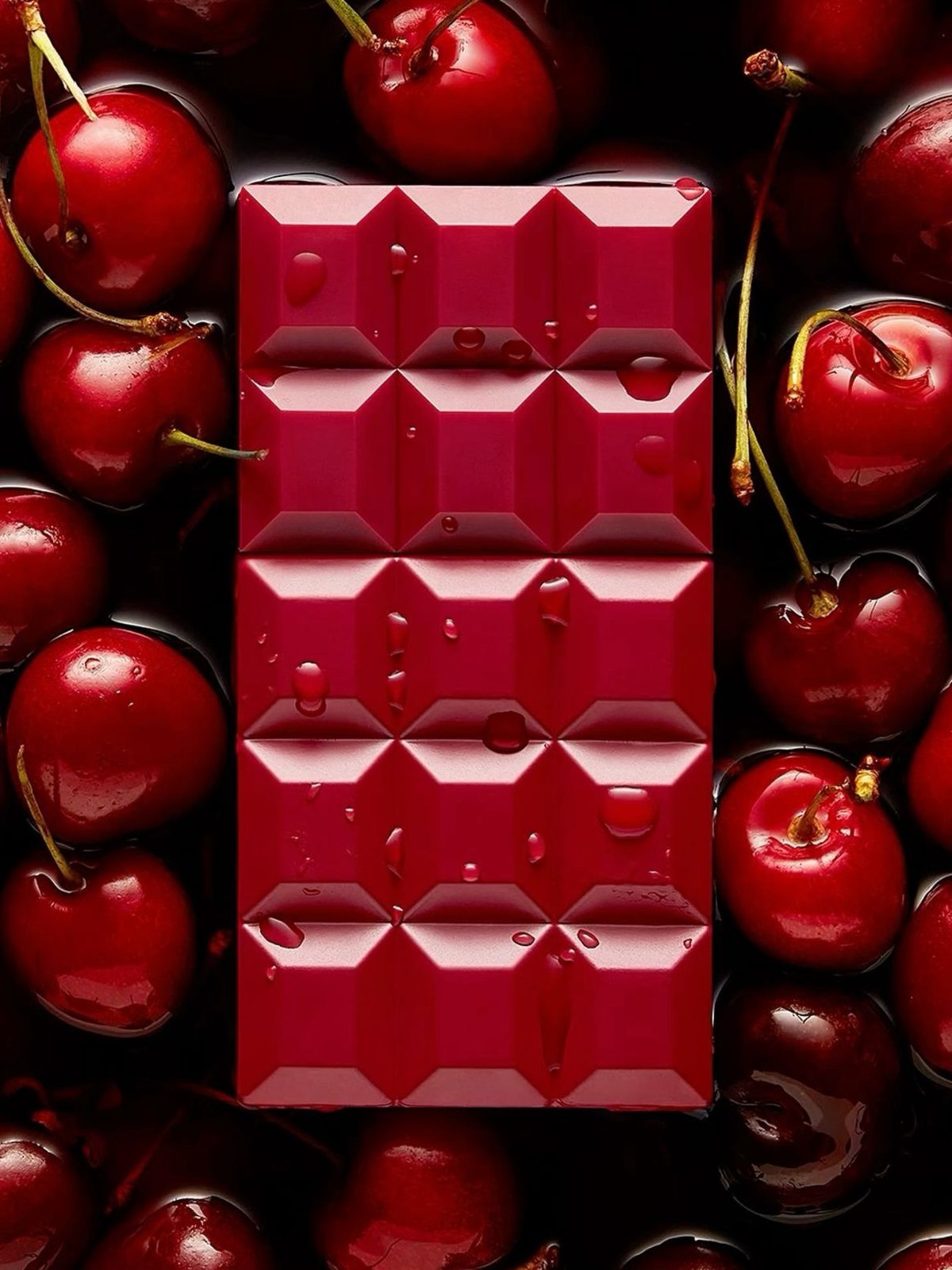 Glossy red chocolate bar surrounded by dark red cherries with water droplets