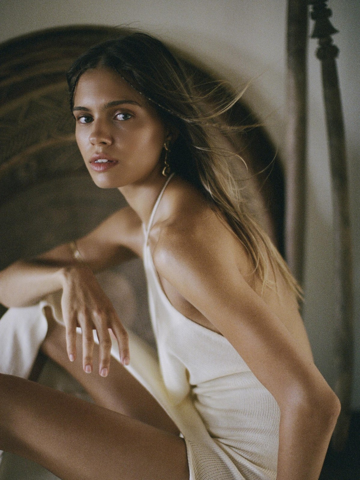Model in an ivory dress seated in a shadowy interior