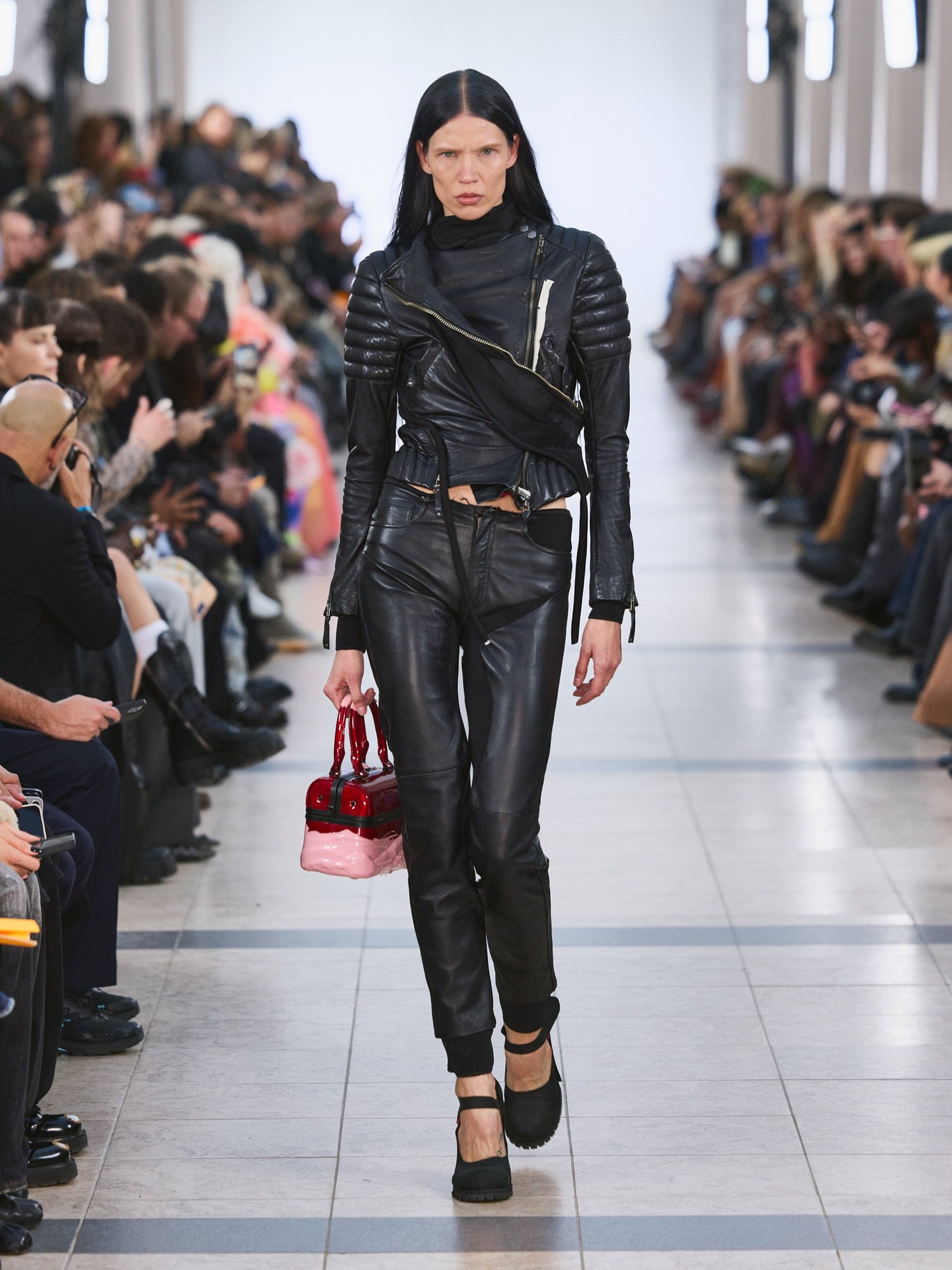 Runway model in a black quilted leather jacket and leather pants with a pink bag