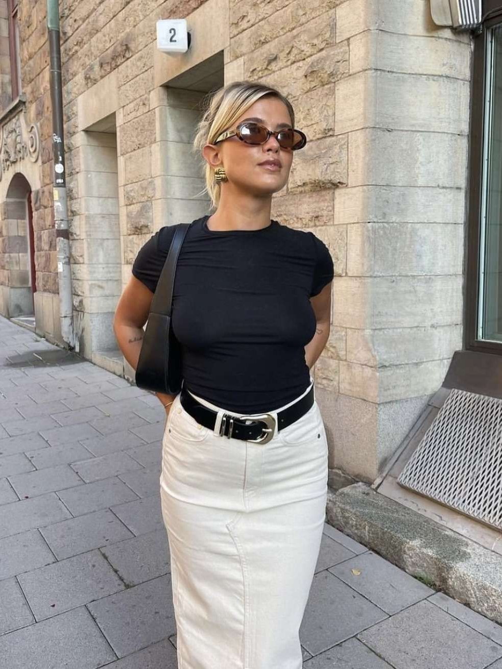 Woman in a black top and white skirt wearing a black belt on a city sidewalk
