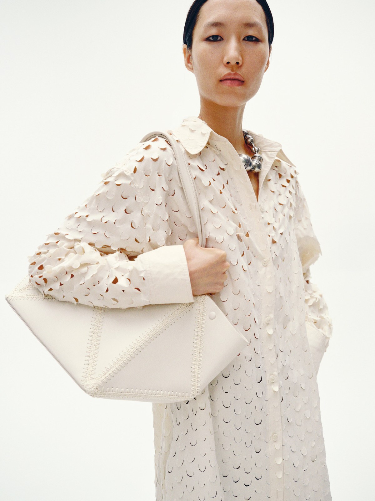 Model in a cream cutwork shirt holding a structured pale bag