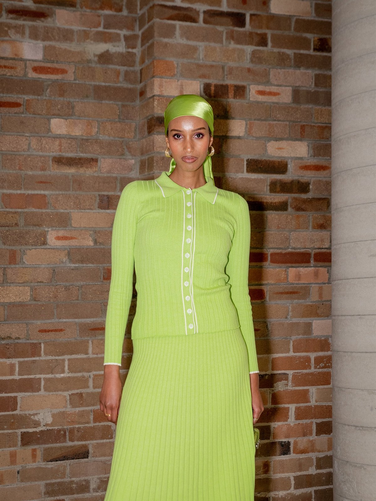 Model in a bright lime ribbed dress at a brick-walled event