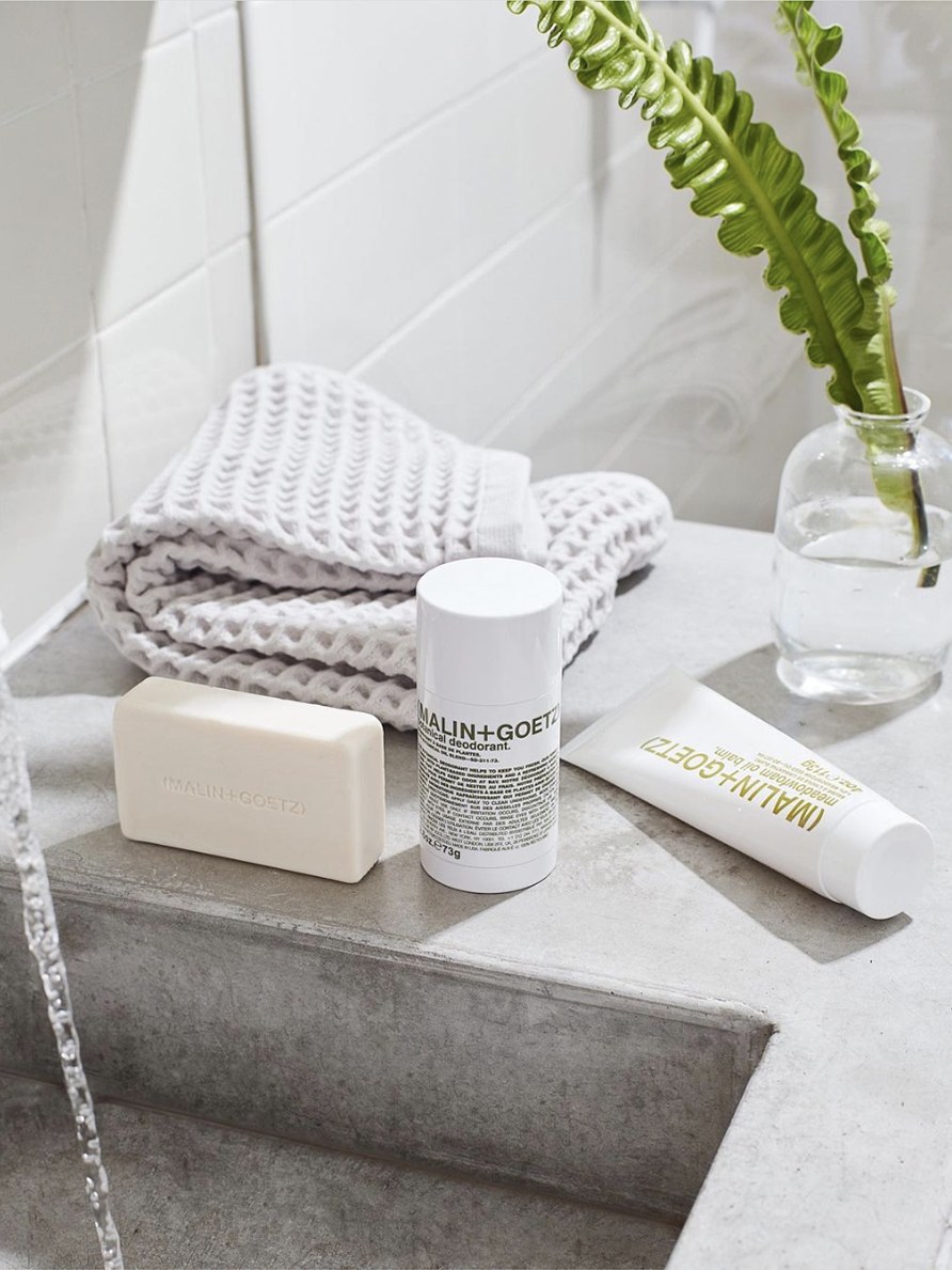 Soap and deodorant on a stone bathroom ledge with folded towels and a plant