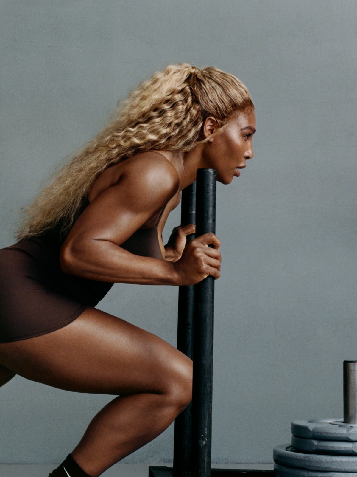 Serena Williams leaning into a lunge beside weight-training equipment