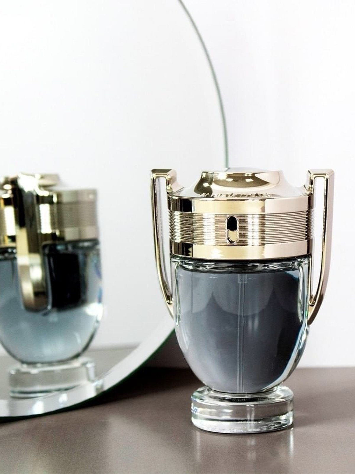 Gold and glass trophy-shaped Invictus bottle on a shelf next to a round mirror