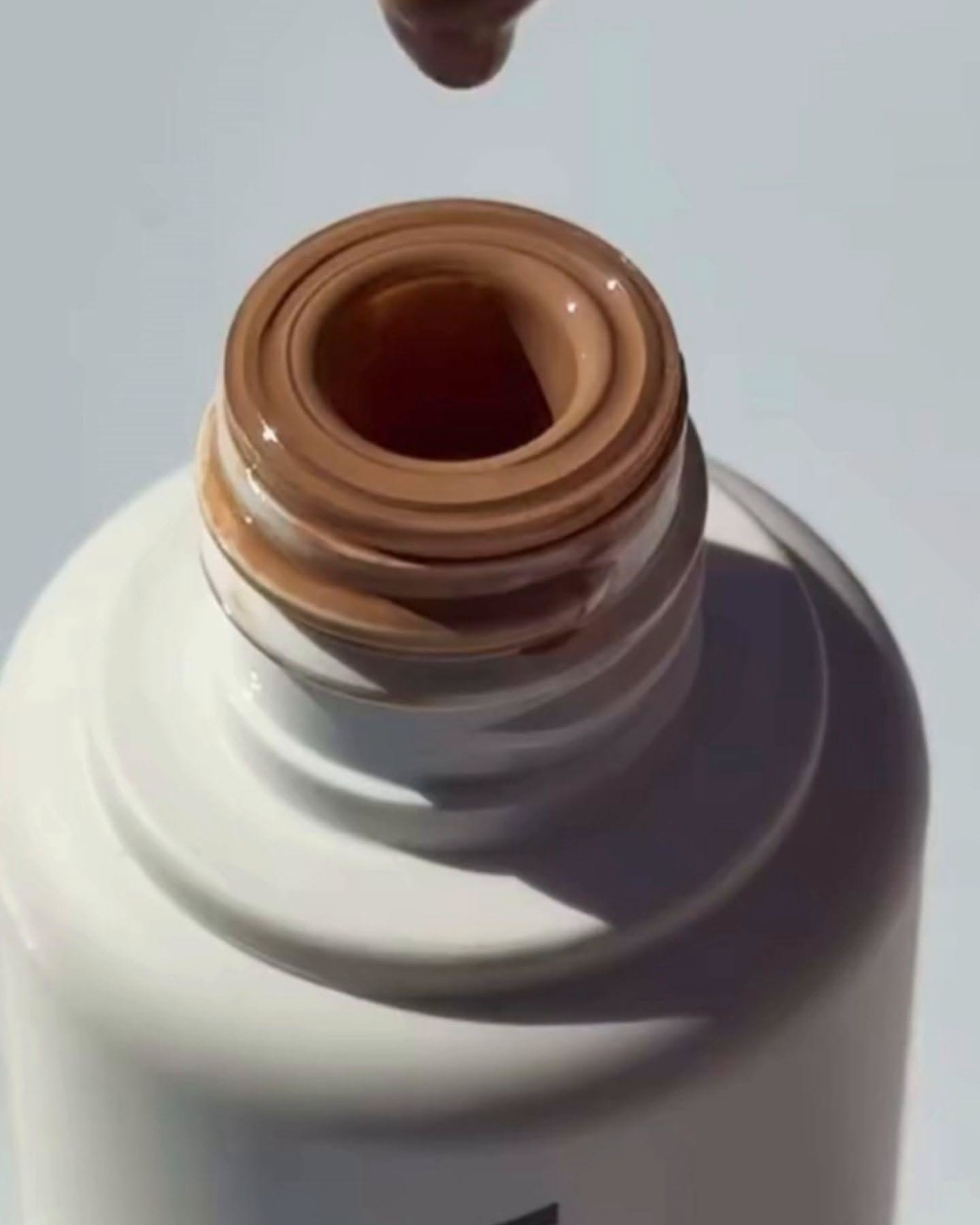 Close-up of a white bottle opening with a drop of medium brown tint dripping into the neck