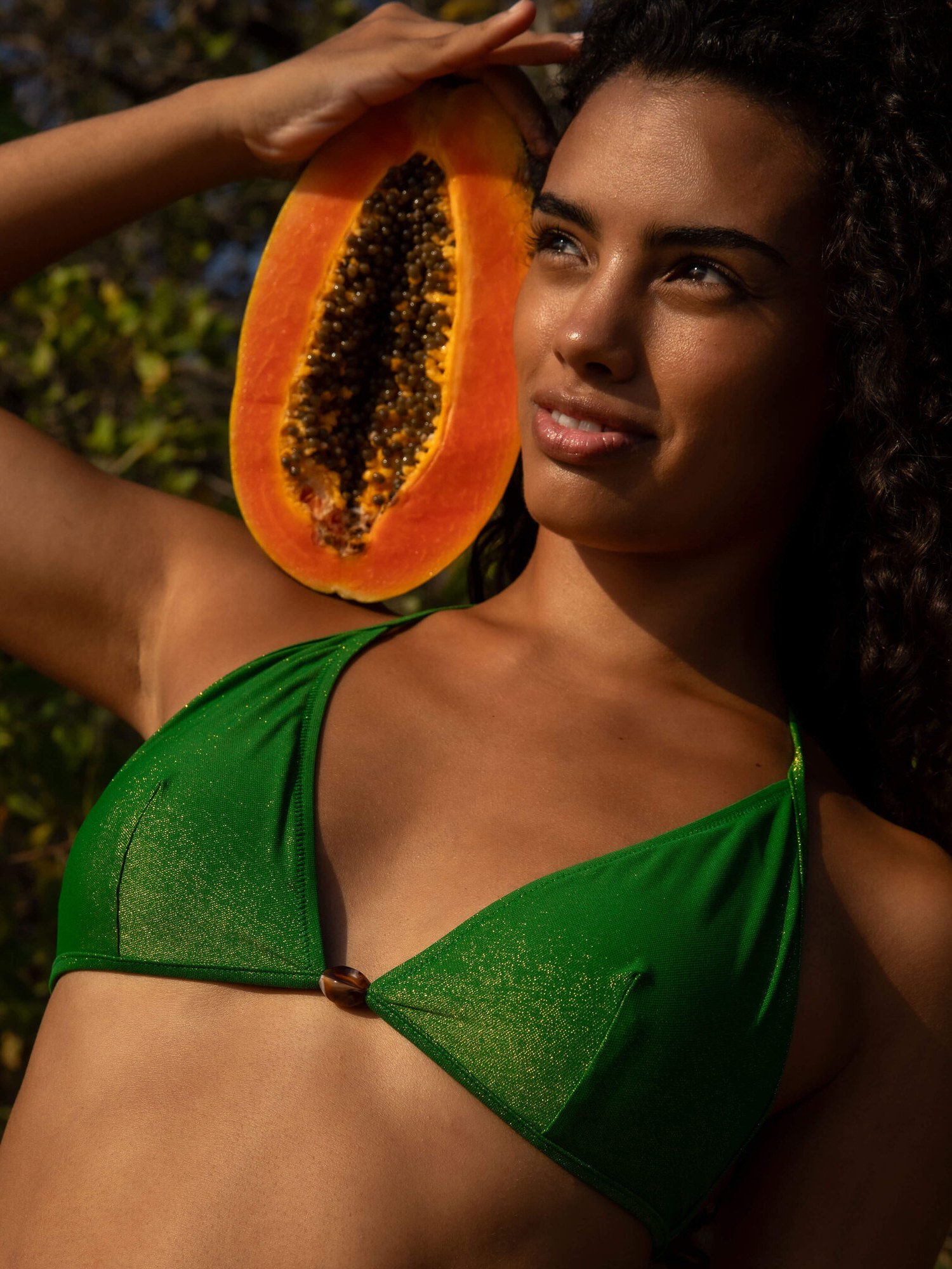 Woman in a green bikini top holding half a papaya