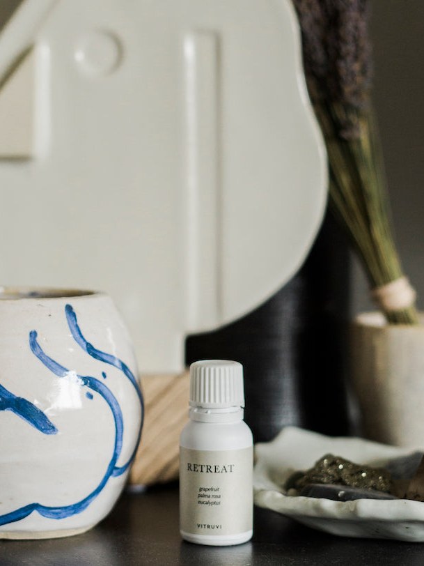 A Vitruvi mist bottle on a home vanity beside a ceramic vessel and greenery