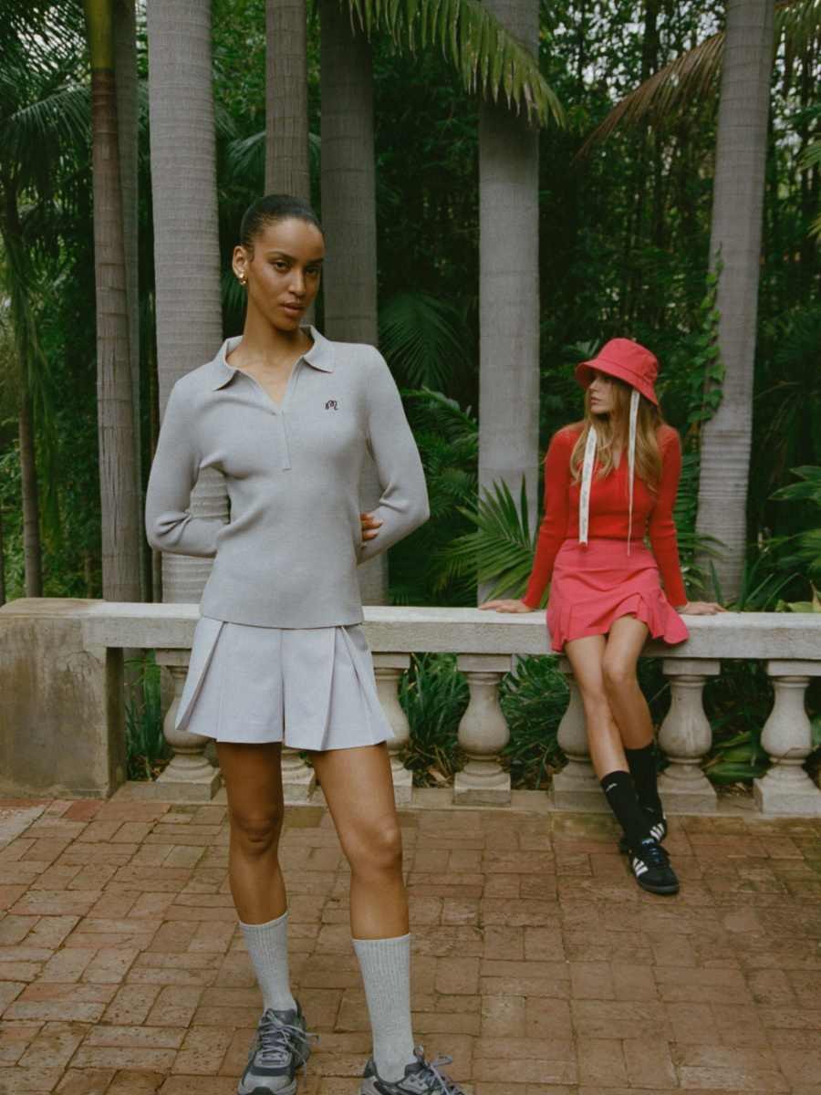 Two women wearing Malbon golf outfits beside a garden terrace