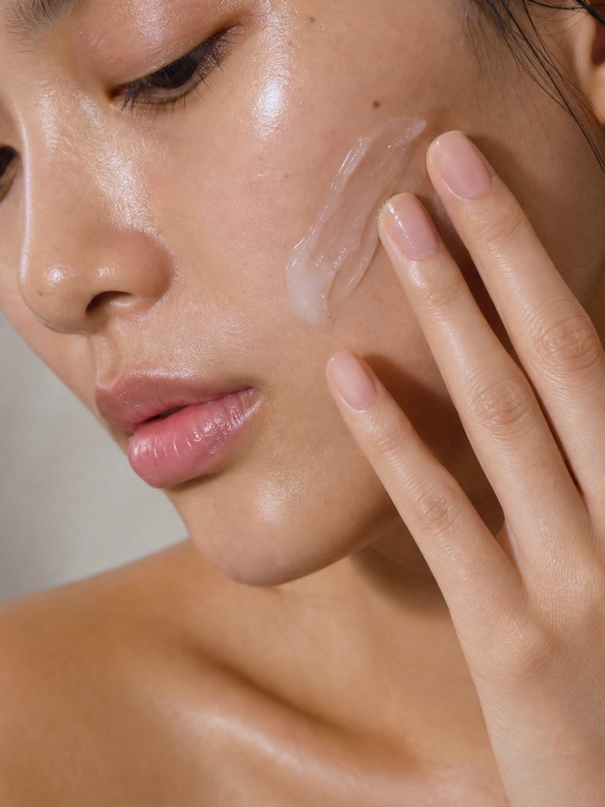 Close-up of a woman's cheek with a smear of clear gel and fingertips touching her face, skin glowing