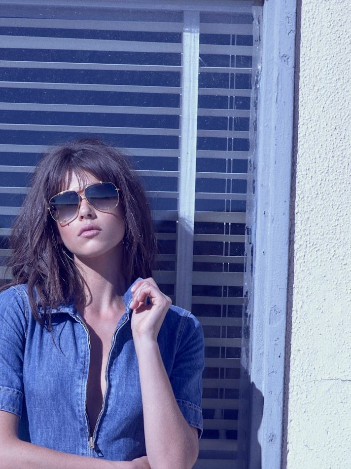 Model in a blue denim jumpsuit and sunglasses beside a storefront