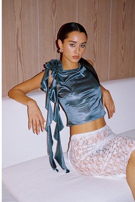 Model seated in a blue satin Lovers and Friends top with ruffle detail