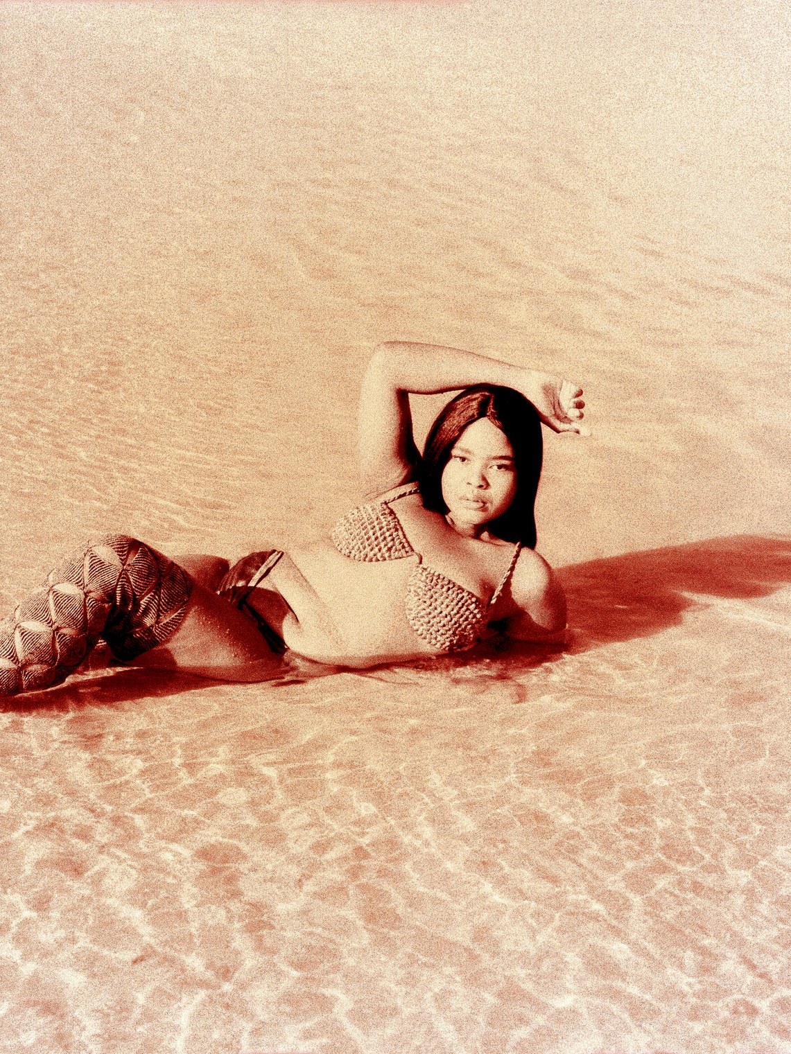 Model reclining in a rust-toned woven swimsuit on sand
