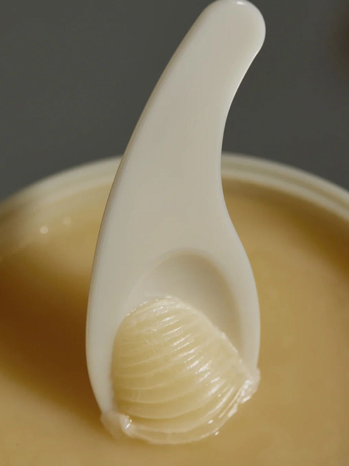 Close-up of an ivory spatula lifting a scoop of pale cleansing balm from a jar