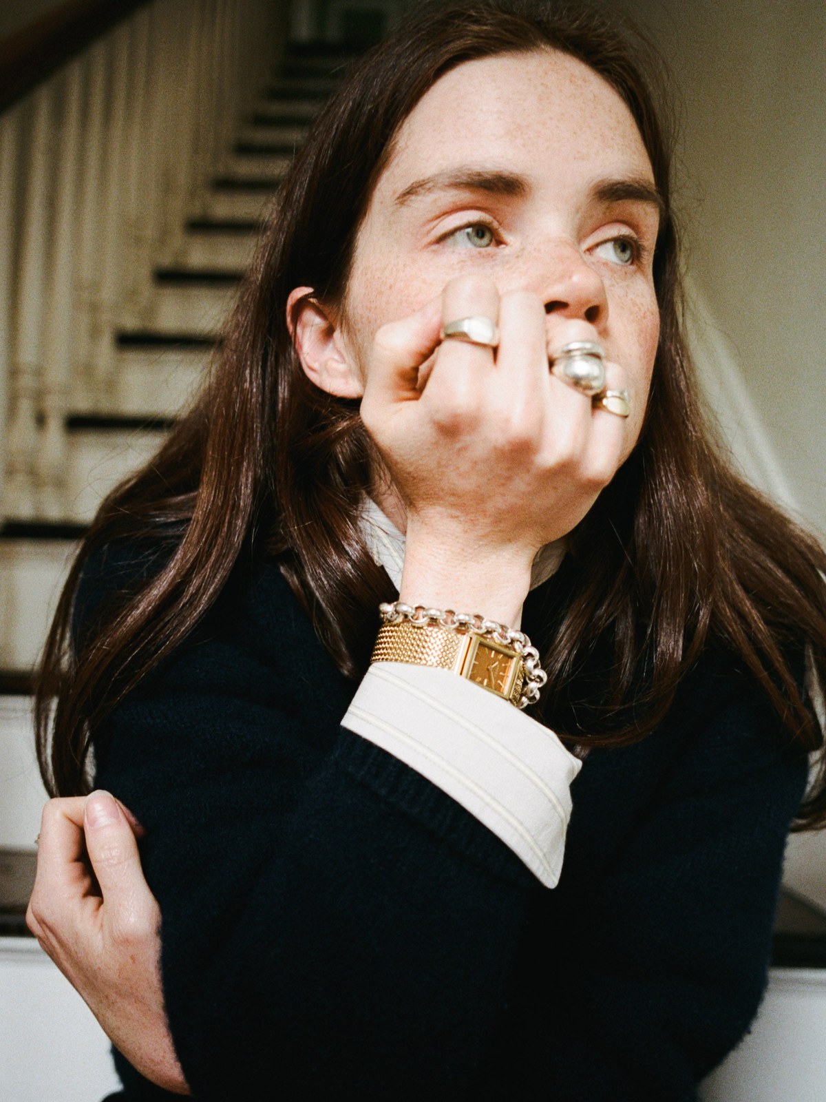 Woman in a dark knit sweater wearing a gold watch near a staircase