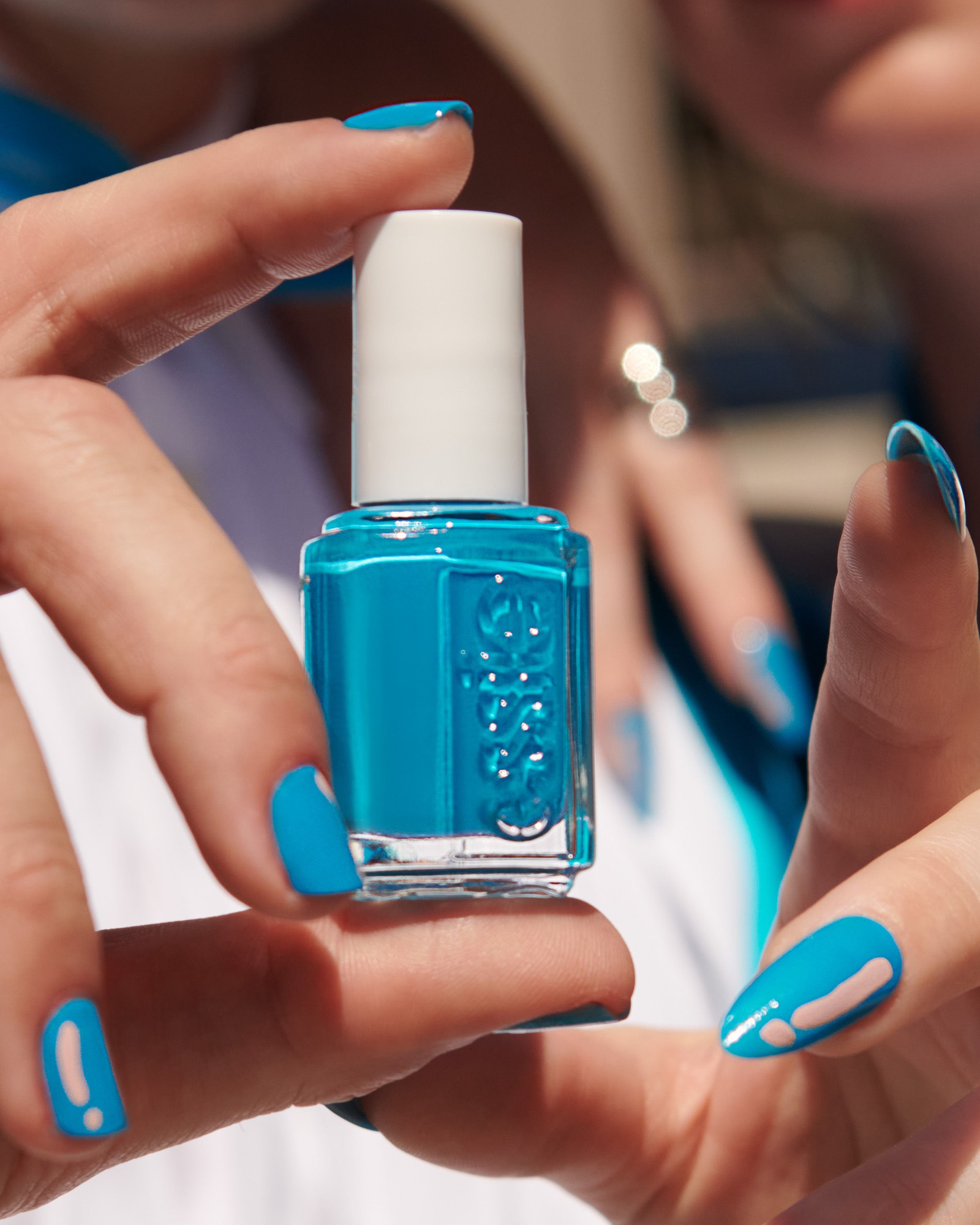 Hand holding a bottle of bright turquoise essie nail polish, the fingernails painted the same colour with a small nude accent