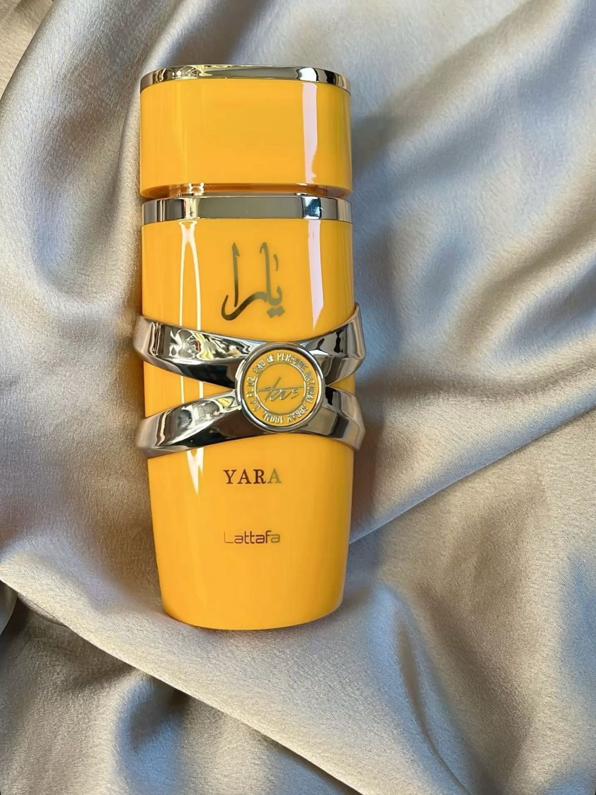 Yellow Lattafa Yara perfume bottle resting on silver satin fabric