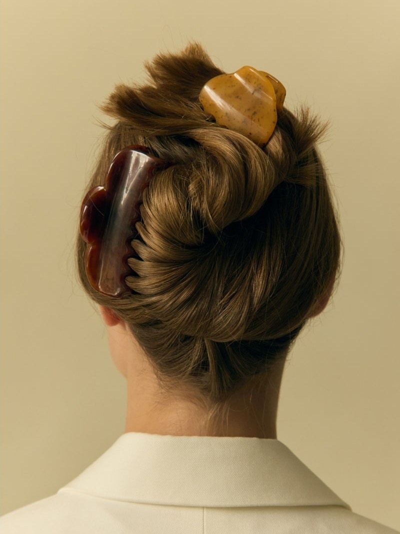 Model with a sculptural claw clip pinning a blonde bun against a pale background