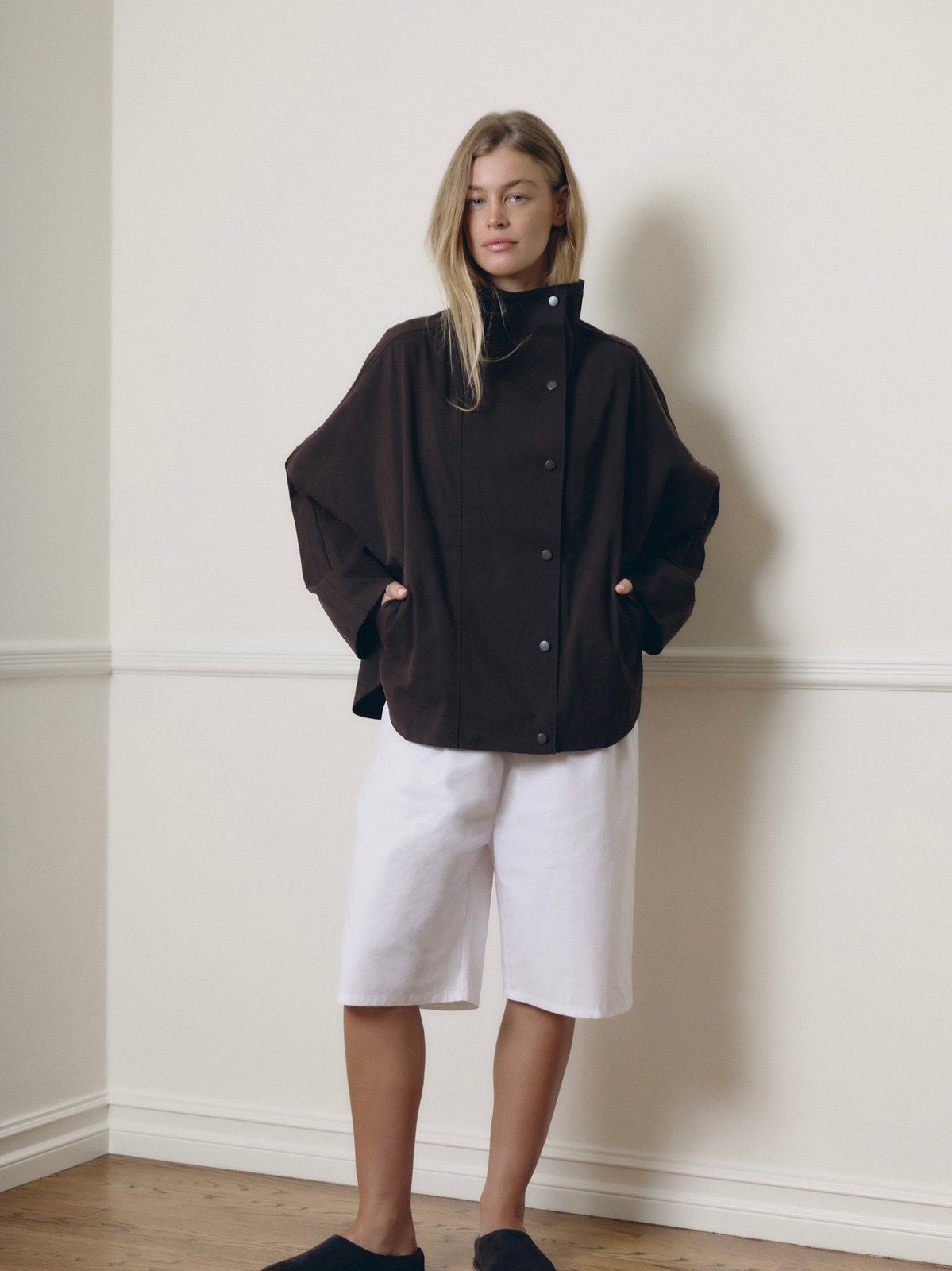 Model wearing a loose dark jacket and white shorts in a minimal studio