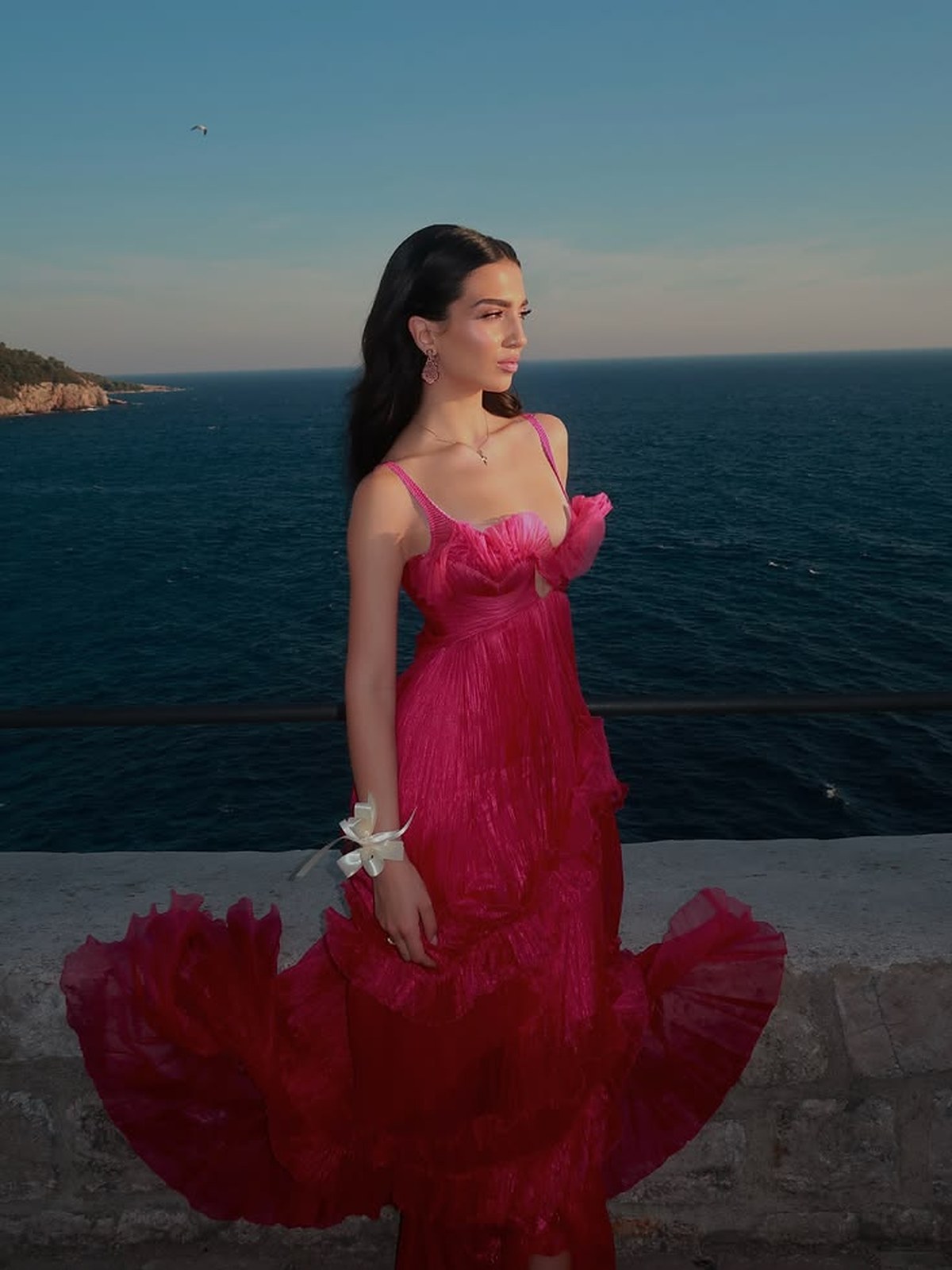Woman in a magenta and red ruffled gown by the sea at sunset