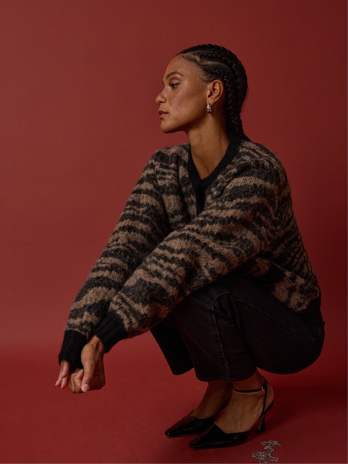 Model in patterned knitwear crouching in profile against a red studio backdrop