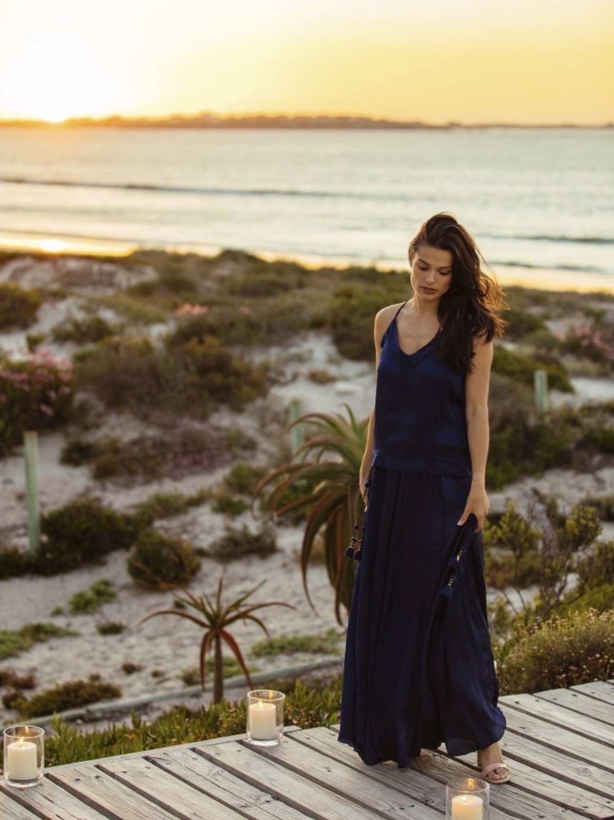 Model in a navy dress on a beachside deck at sunset