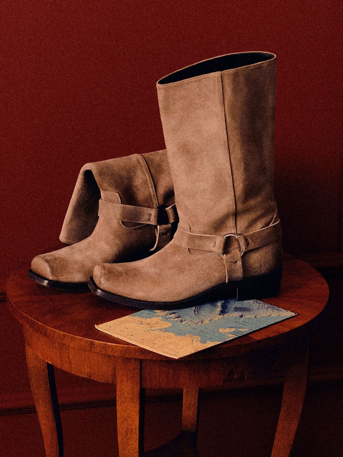 Tan suede Golden Goose buckle boots on a wooden table against a red wall