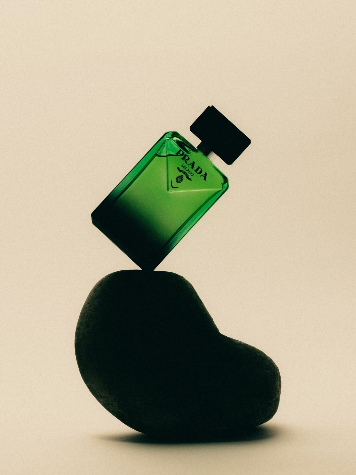 Green Prada Milano perfume bottle balanced on a dark stone against a cream background