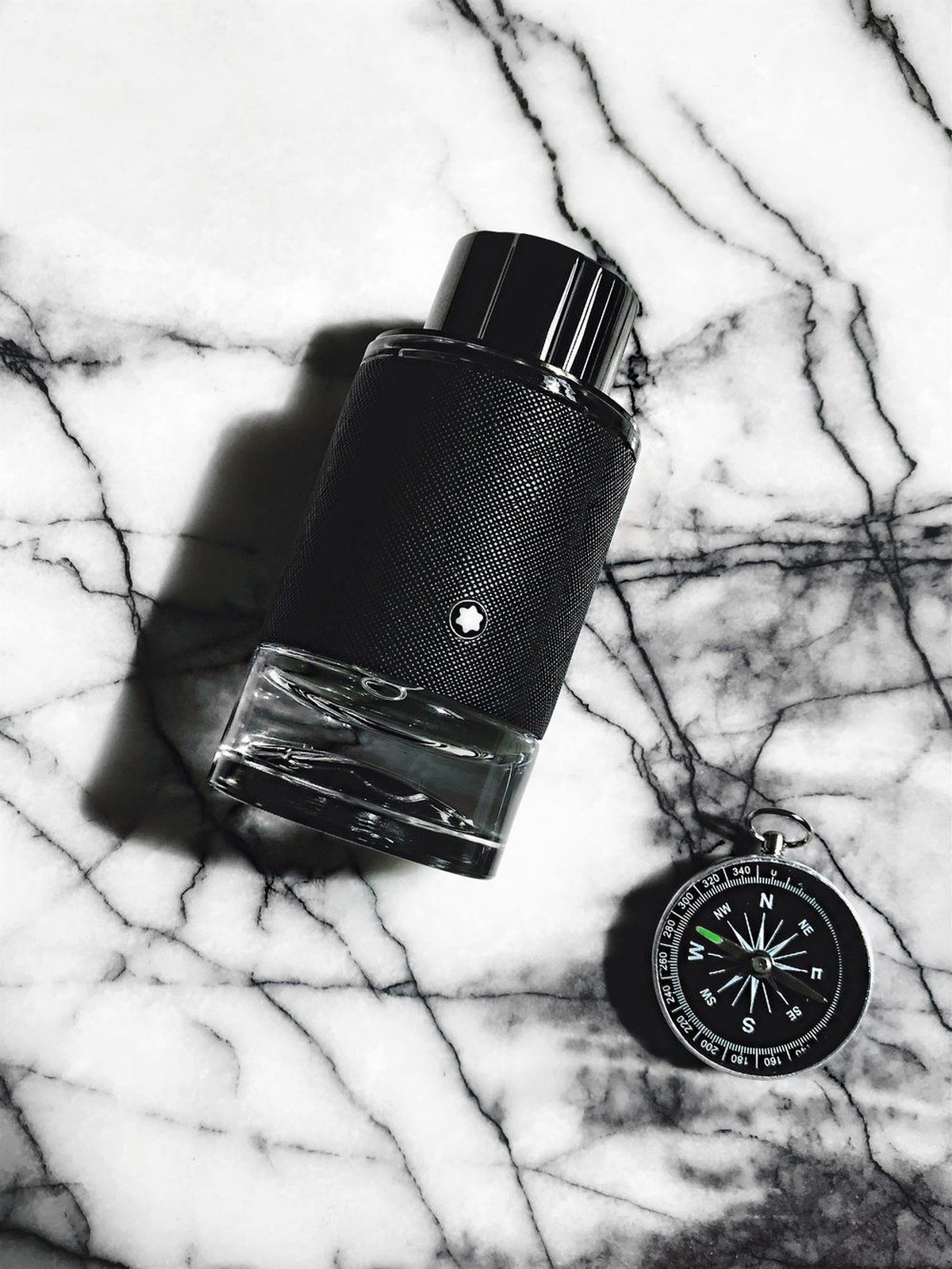 Montblanc Explorer bottle lying on black and white marble beside a small compass