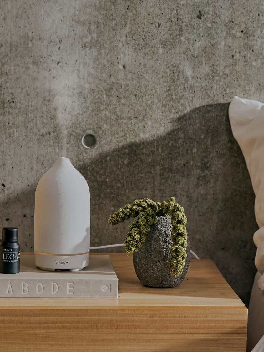 White Vitruvi diffuser on a bedside table beside a plant and pale bedding