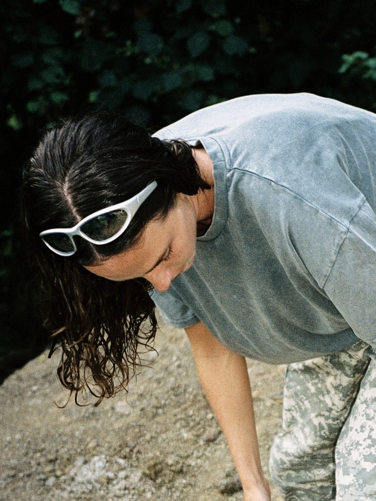 Woman in white Chimi sunglasses bending outdoors beside greenery