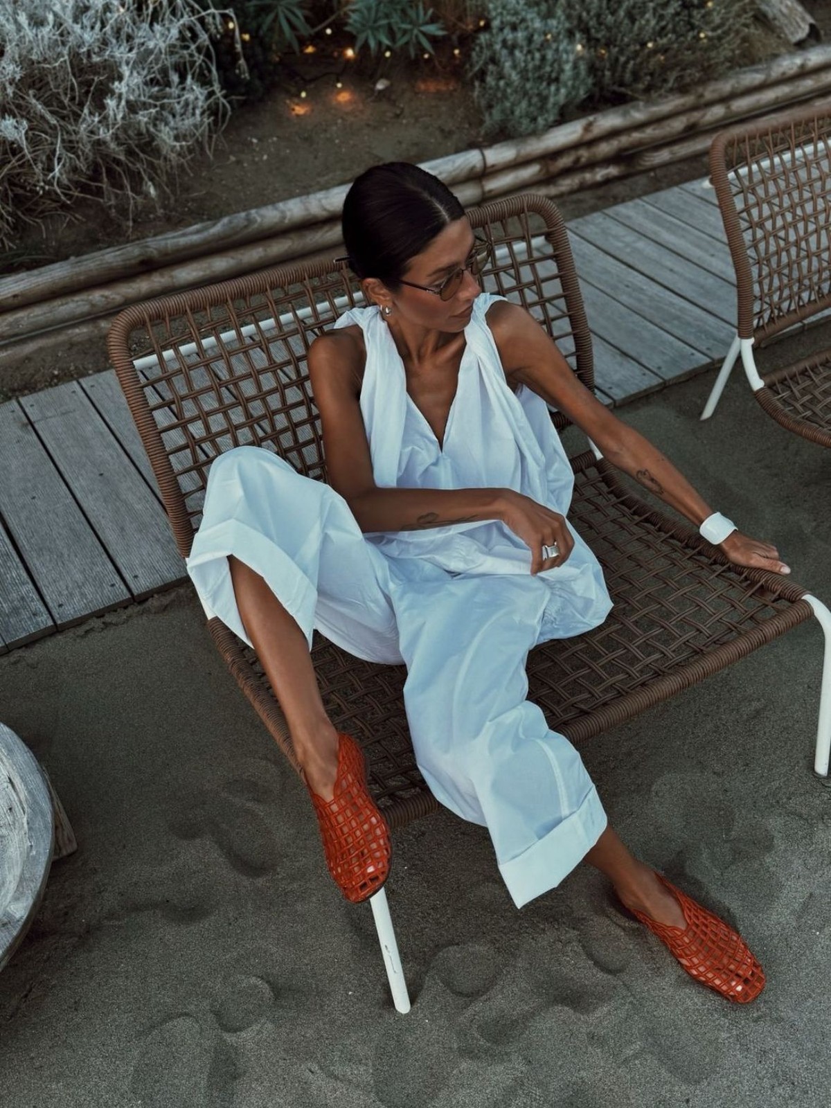 Woman in a white linen jumpsuit and orange woven mules sitting in a beach chair