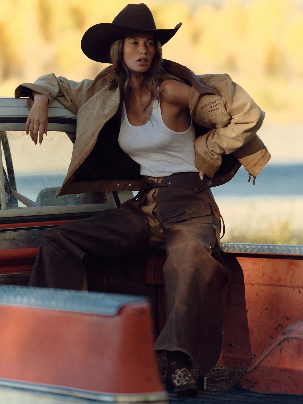 Model in an embroidered Diamond Cross Ranch jacket and cowboy hat beside a truck.