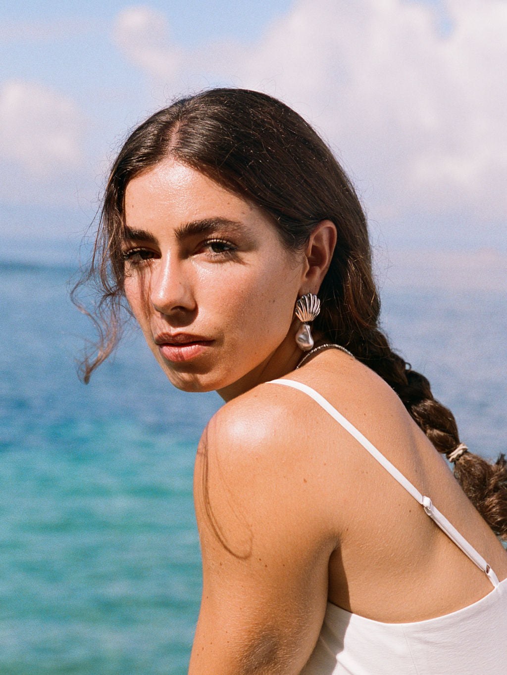 Model in a white top wearing sculptural earrings by the water