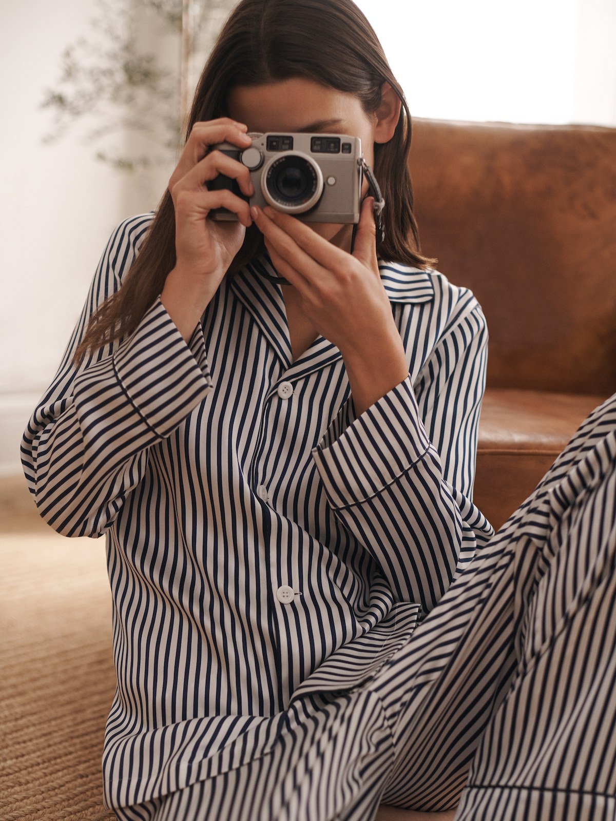 Woman in striped pajamas holding a camera in front of her face in a softly lit bedroom
