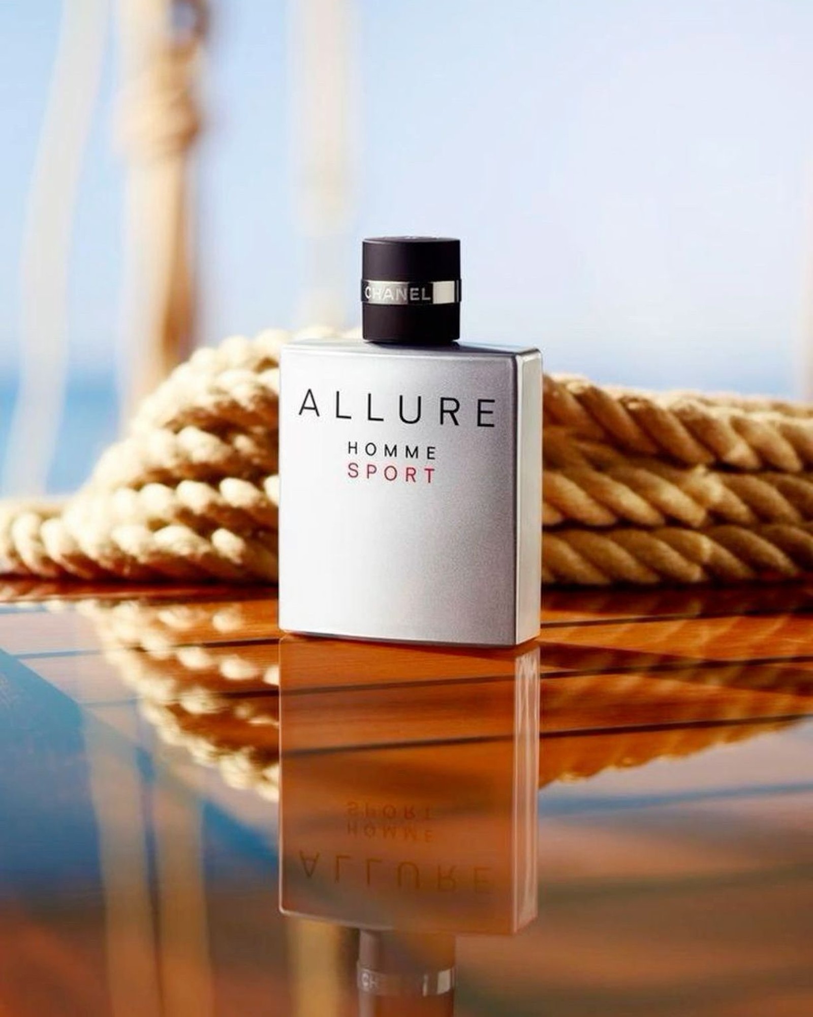 Silver Chanel Allure Homme Sport bottle with a black cap resting on a varnished wood surface beside coiled rope