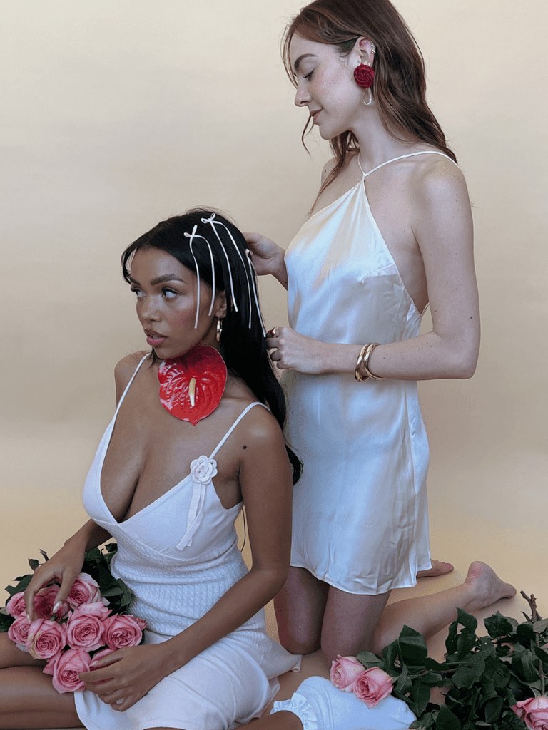 Two models in white looks wearing colorful statement earrings and bracelets among roses